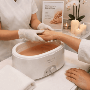 Immagine di una estetista in camice bianco che faun bagno di paraffina liquida alle mani di una cliente in un centro estetico.