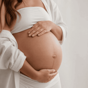 Immagine di giovane donna incinta, vestita di bianco, che si abbraccia la pancia scoperta.