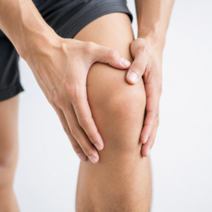 Primo piano della gamba di un giovane uomo in pantaloncini neri che si massaggia un ginocchio con le mani.