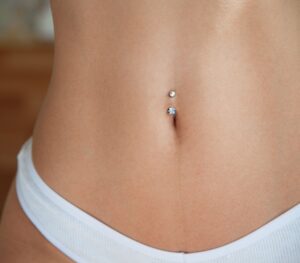 Primo piano della pancia tonica di una giovane donna in slip bianco con piercing all'ombelico.