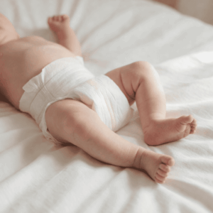 Primo piano delle gambe di un neonato, sdraiato su lenzuola bianche, che indossa un pannolino.