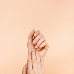 Primo piano delle mani di una giovane donna, con unghie molto curate e french manicure su sfondo rosa uniforme.